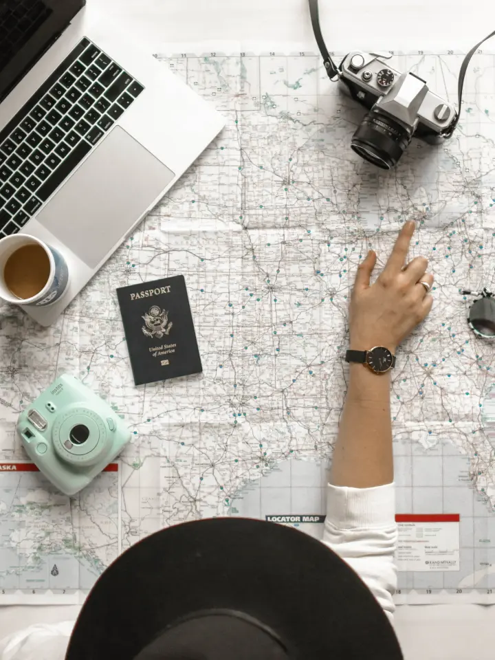 Hand pointing at city on map spread out on desktop with computer coffee passport | Salt Lake City Apartments